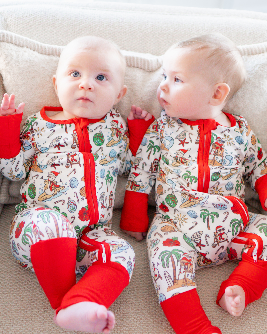 Two babies sitting in a couch wearing matching holiday pajamas